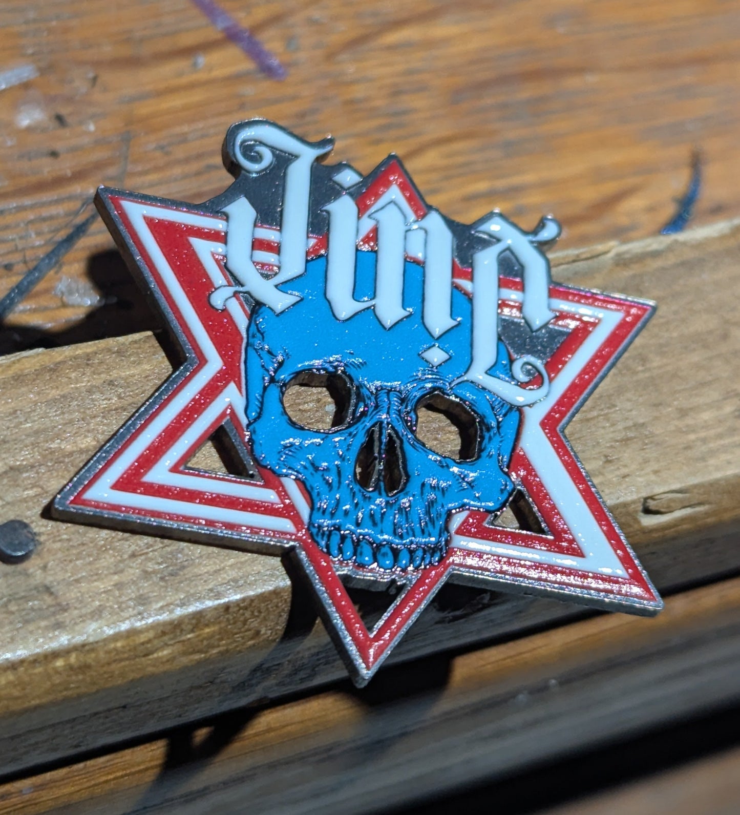 Star-shaped badge with skull design and 'JINX' text on a wooden surface